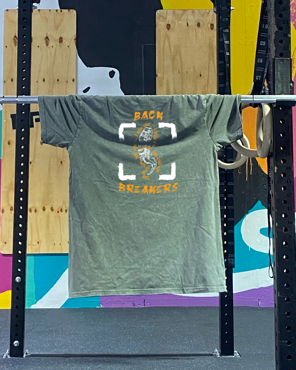 stone wash leger groene t shirt, hangt op een barbell in een crossfit box, heeft een twee kleuren print aan de achterkant